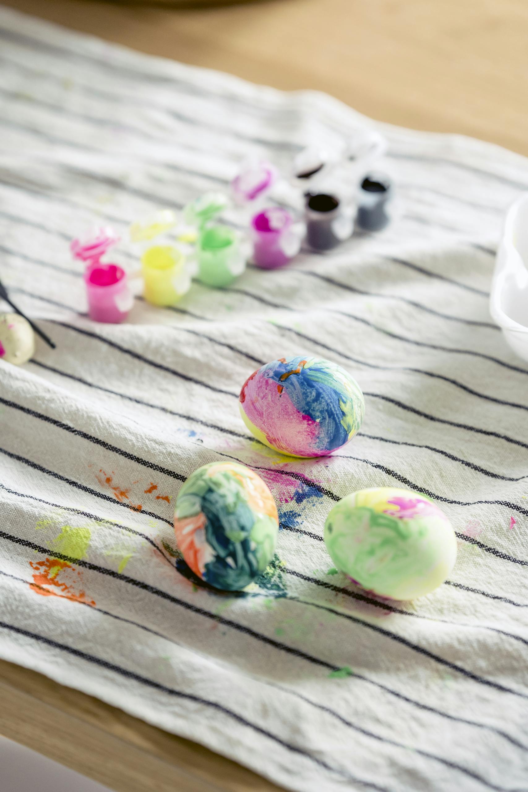 Colorful Easter eggs drying on a striped cloth with vibrant paint jars nearby, perfect for festive decor.